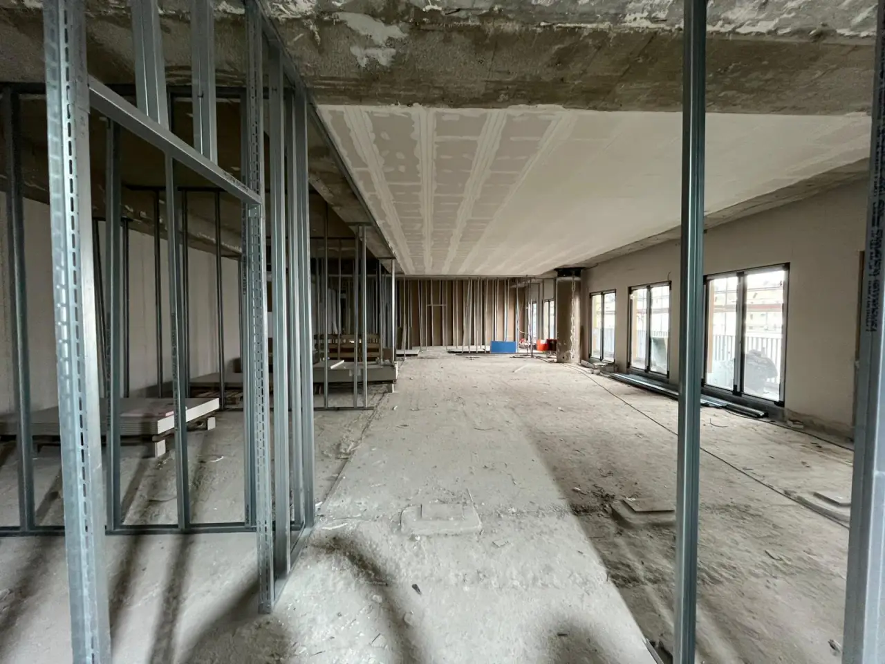 Großer Raum im Rohbau mit Ständerwerk und durchgehender Fensterfront, Bauphase März 2026